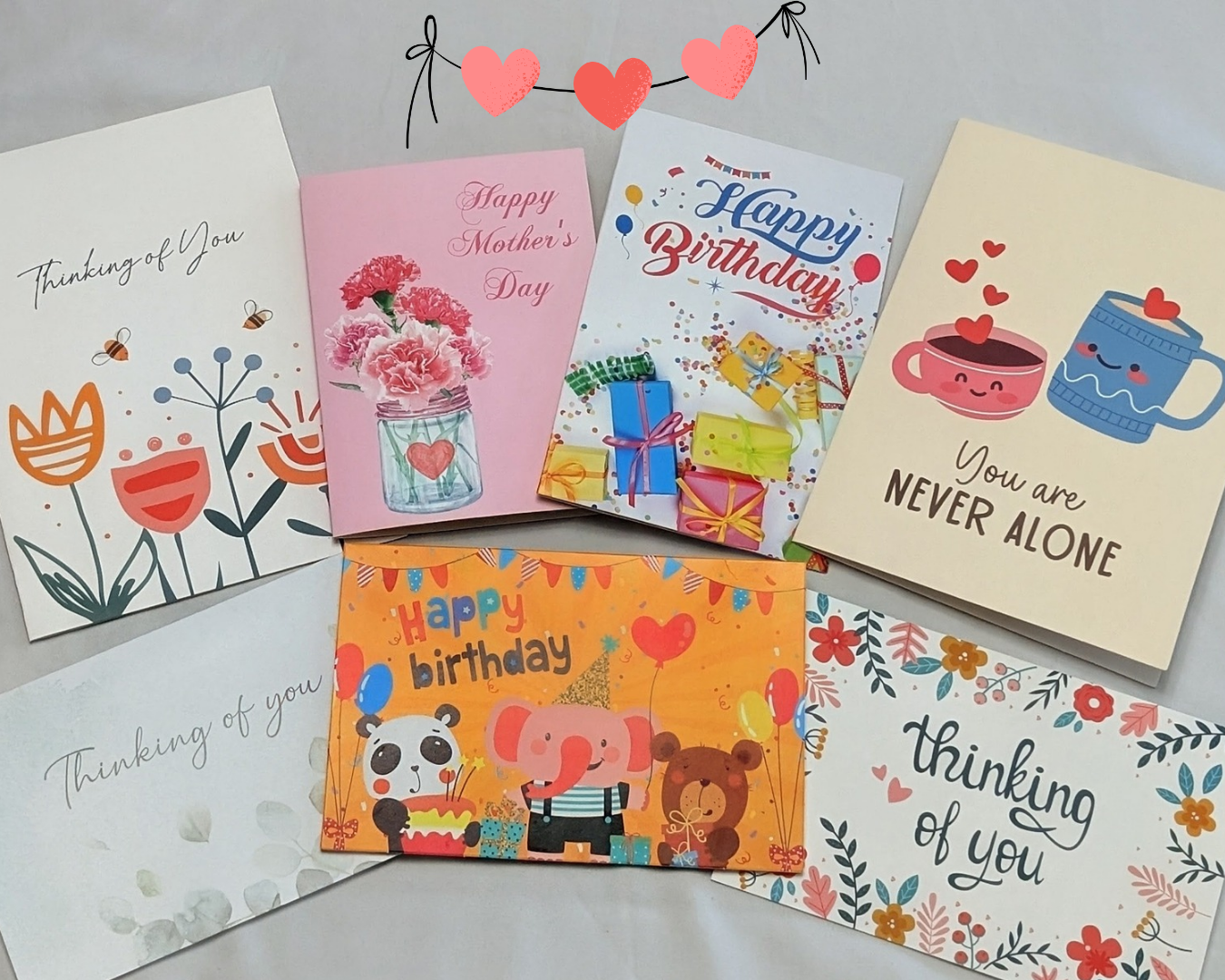 A grid of thinking-of-you and holiday cards laid out on white fabric — florals, birthday designs, and Mother's Day