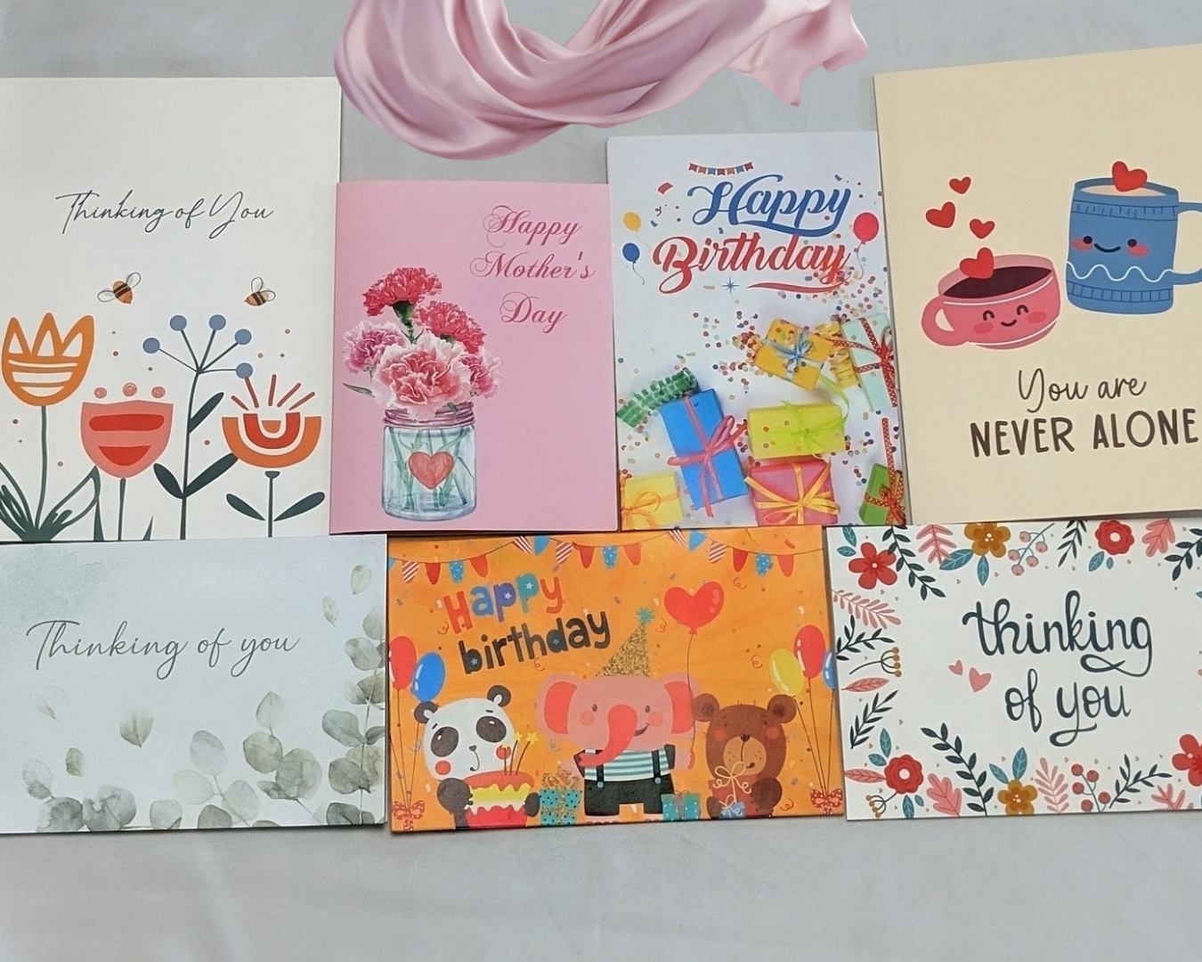 A fan of hand-picked greeting cards from a Love Posted packet — birthday, Mother's Day, and thinking-of-you designs laid out on soft white fabric