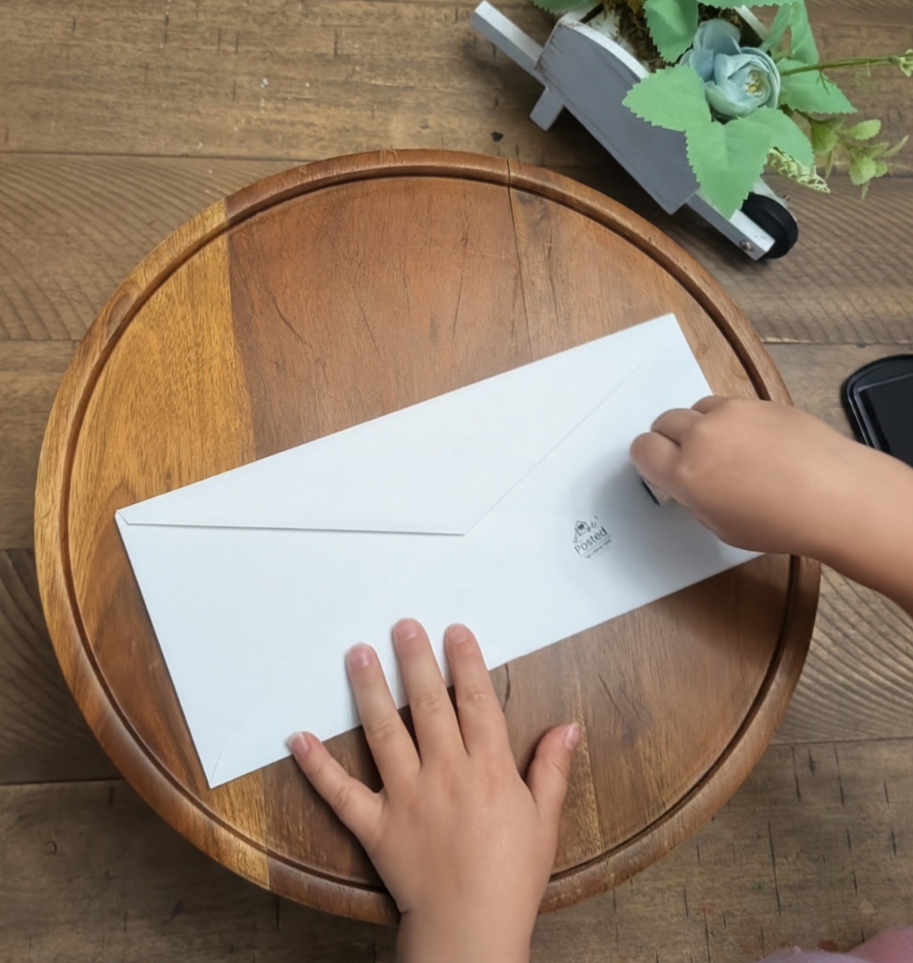 A child pressing the flap closed on a sealed white envelope at the kitchen table